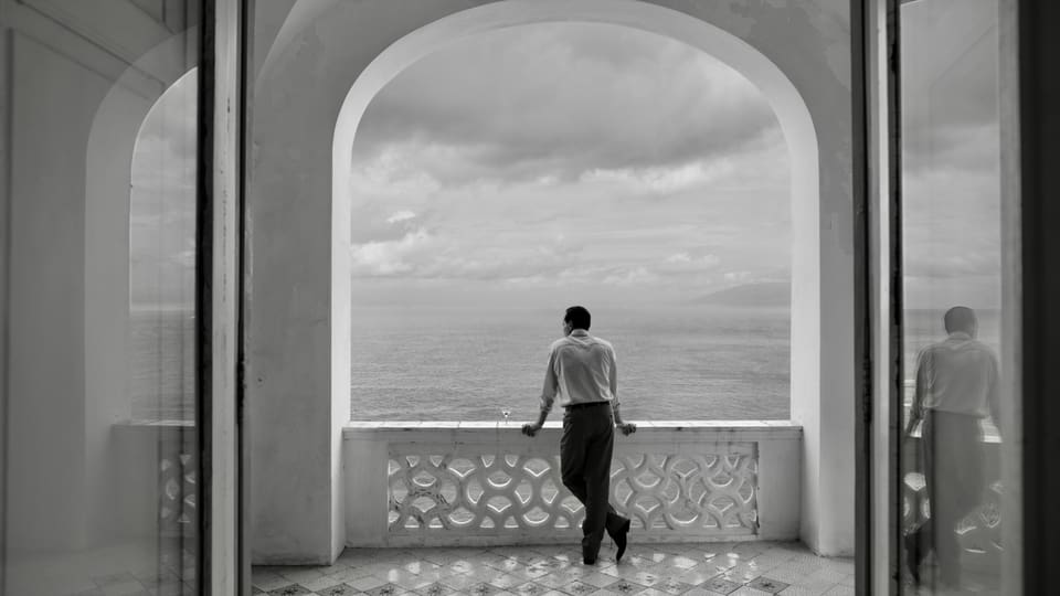Mann schaut von einem Balkon aufs Meer.