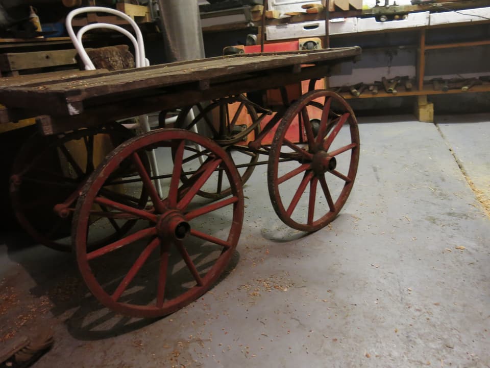 Ein Holzwagen mit vier Rädern steht auf einem BEtonboden. 