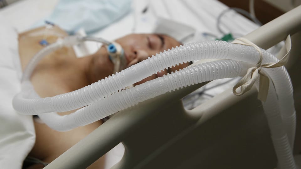 Ein Mann mit Beatmungsschlauch im Mund liegt im Spitalbett.