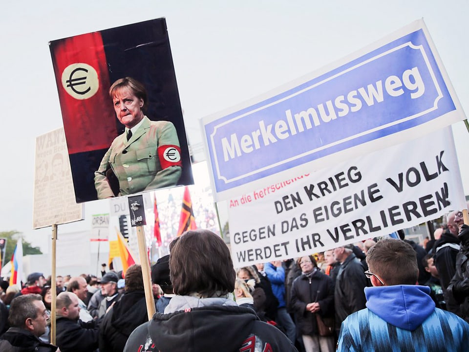 Plakat mit einer Montage, auf der die deutsche Bundeskanzlerin Merkel in naziähnlicher Uniform zu sehen ist. Daneben ein anderes Plakat: Merkel muss weg. 