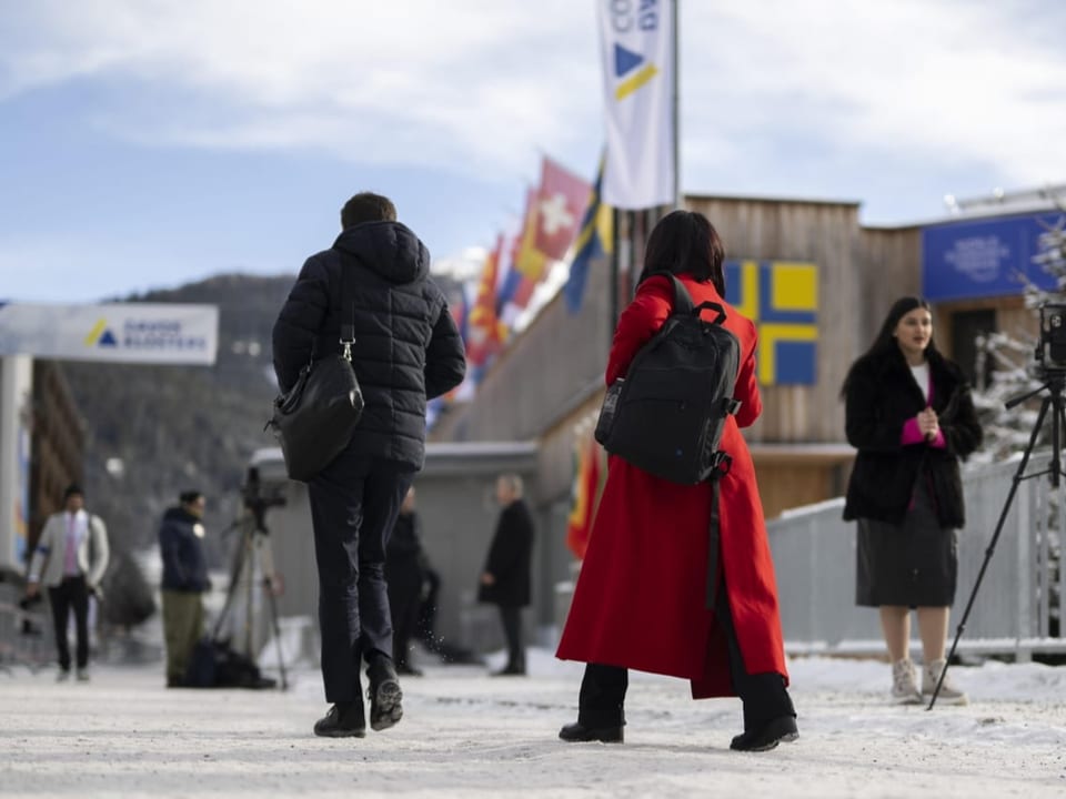 Personen laufen auf einem verschneiten Platz. Im Hintergrund Journalistinnen mit Kameras.