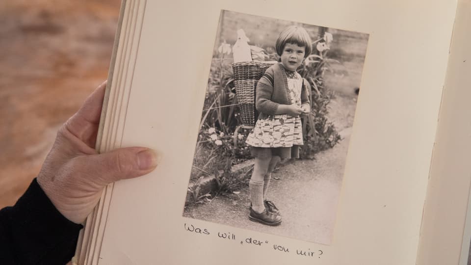 Blick in ein Fotoalbum: Eine Schwarz-Weiss-Aufnahme zeigt ein kleines Mädchen mit einem Korb auf dem Rücken. 