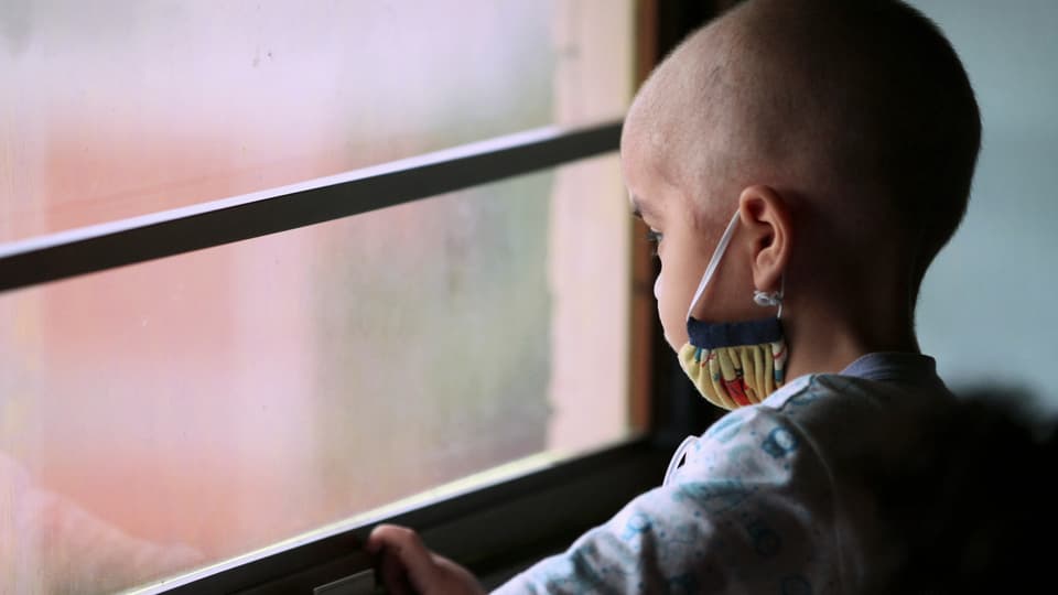 Ein an Krebs erkranktes Kind schaut aus dem Fenster.