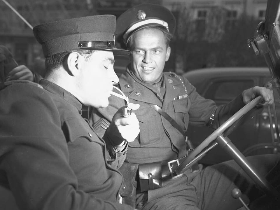 Ein uniformierter Mann zündet einem anderen uniformierten Mann im Jeep eine Zigarette an.