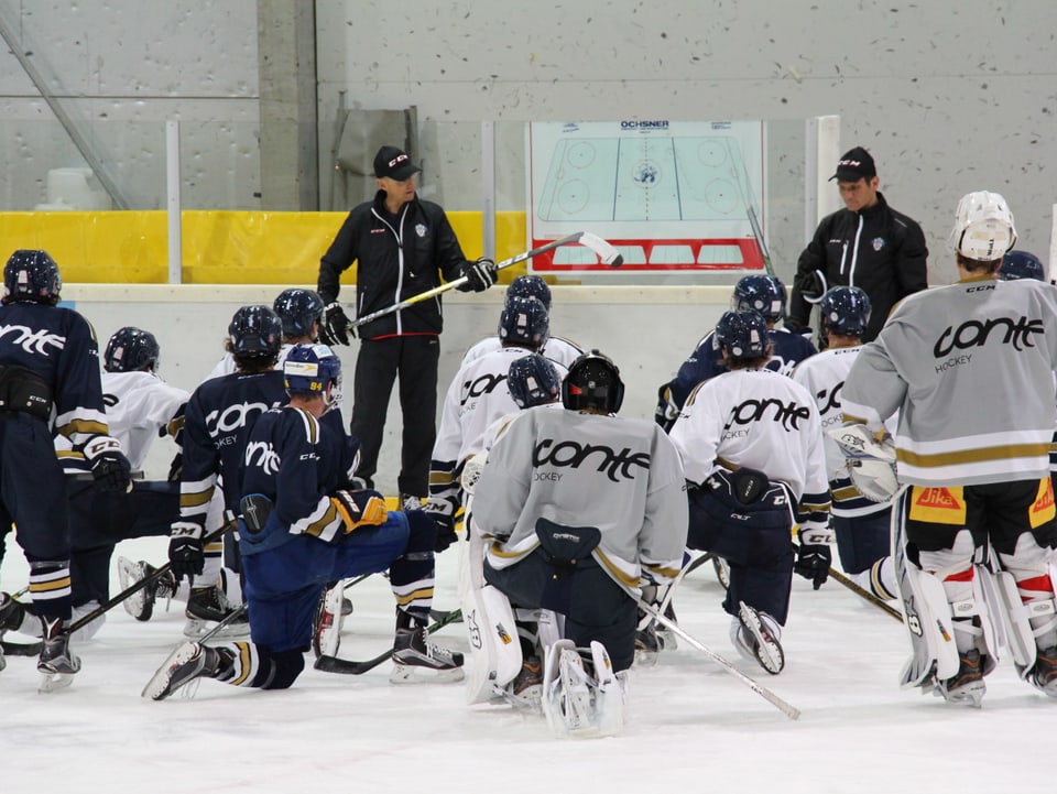 Eishockey-Spieler kauern vor ihren Trainern auf dem Eis.