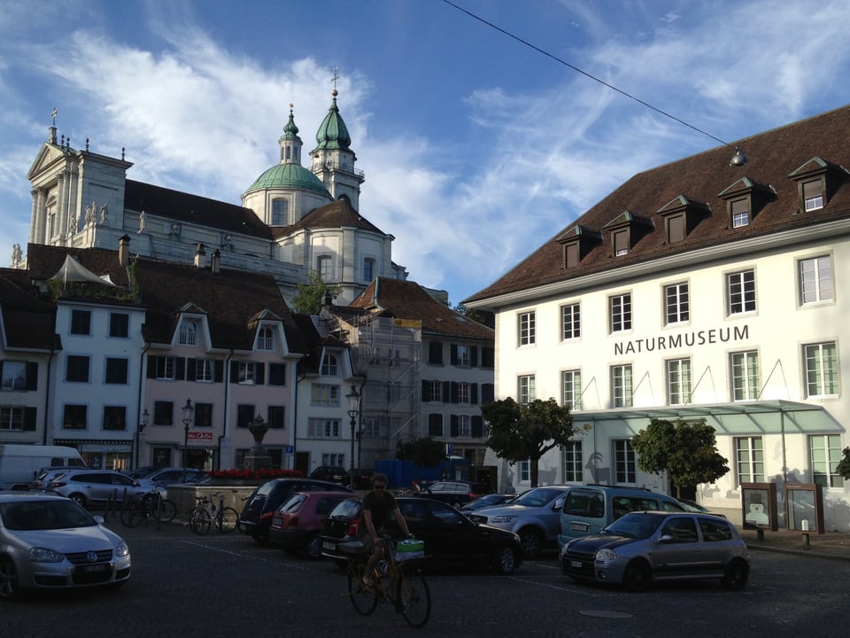 Parkplatz auf dem Klosterplatz, im Hintergrund der Eingang zum Naturmuseum und links davon die Kathedrale, die in den Himmel ragt.