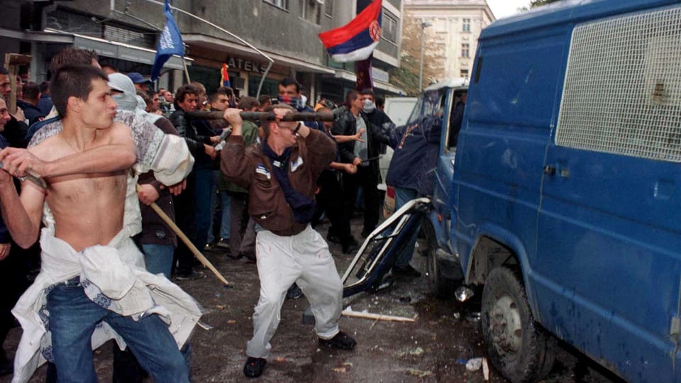 Ein Polizeifahrzeug wird von bewaffneten Demonstranten attackiert.