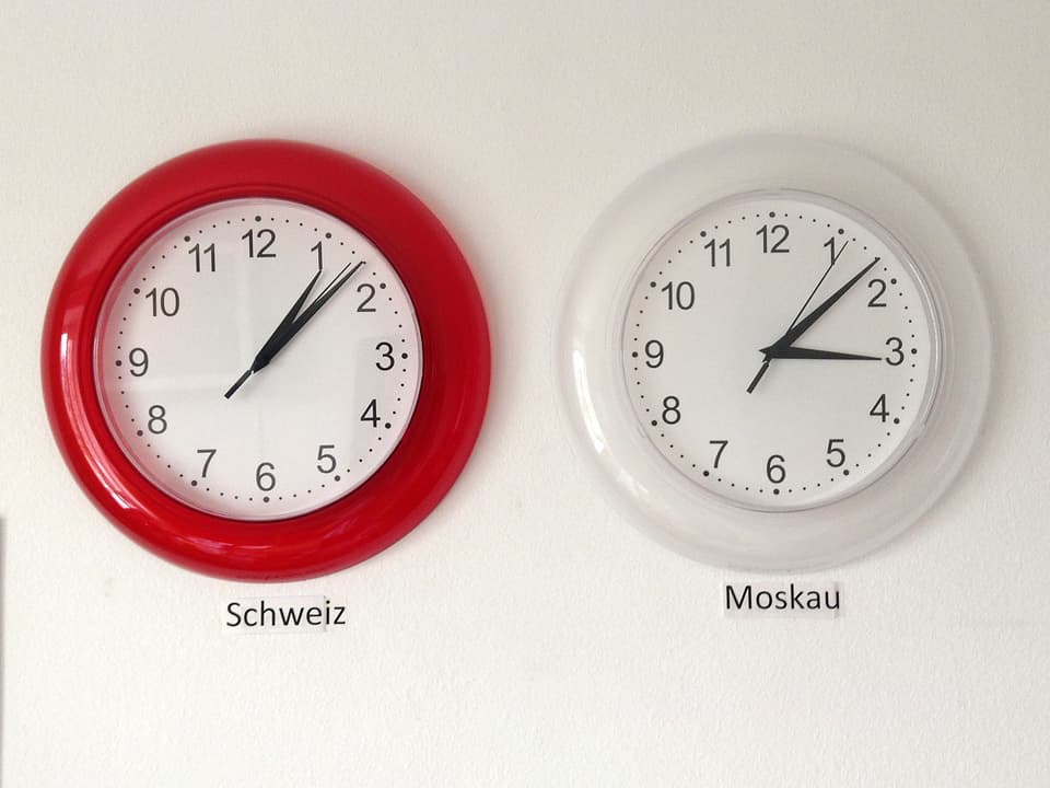 Eine rote Wanduhr mit Schweizer Zeit, rechts daneben eine weisse mit Moskauer Zeit.