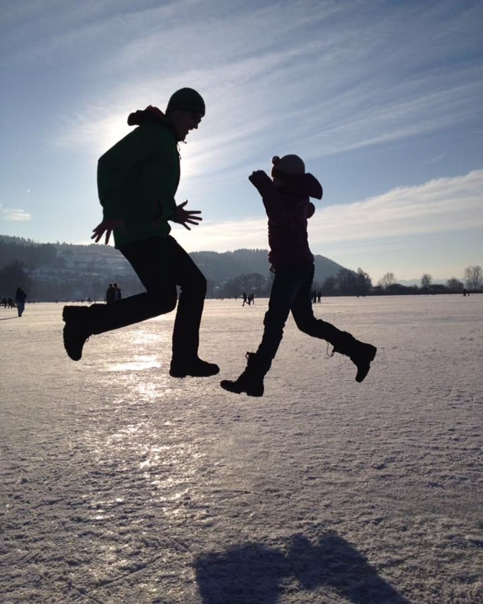 Zwei Menschen springen auf der Eisfläche des Mauensees in die  Luft.
