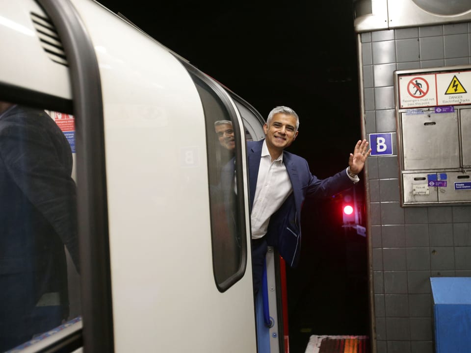 Sadiq Khan winkt aus einem U-Bahn-Waggon heraus in die Kamera.
