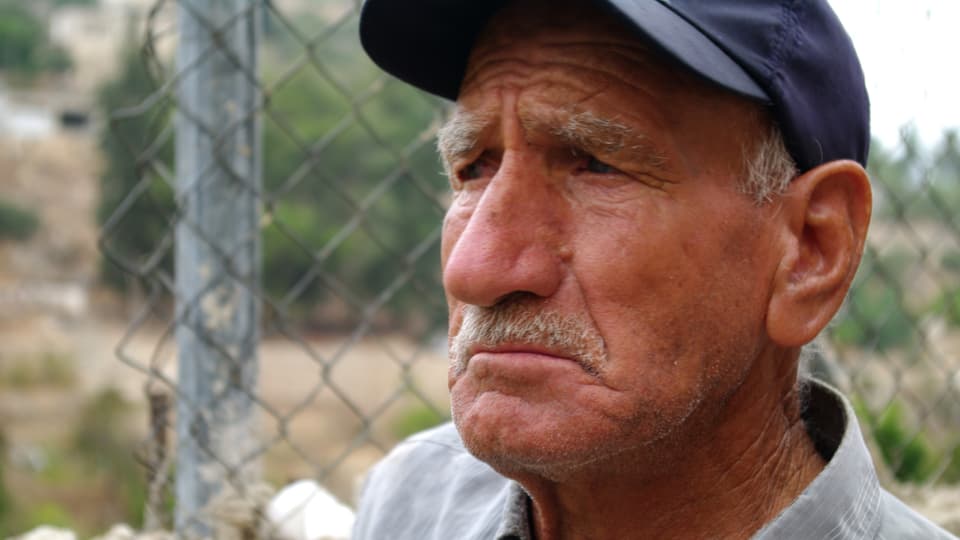 Ein älterer Mann mit Oberlippenbart und Dachkappe, leicht traurig und verbittert in die Ferne schauend.