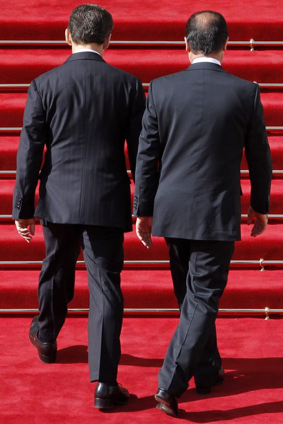 Hollande und Sarkozy stehen vor einer Treppe. Von hinten fotografiert.