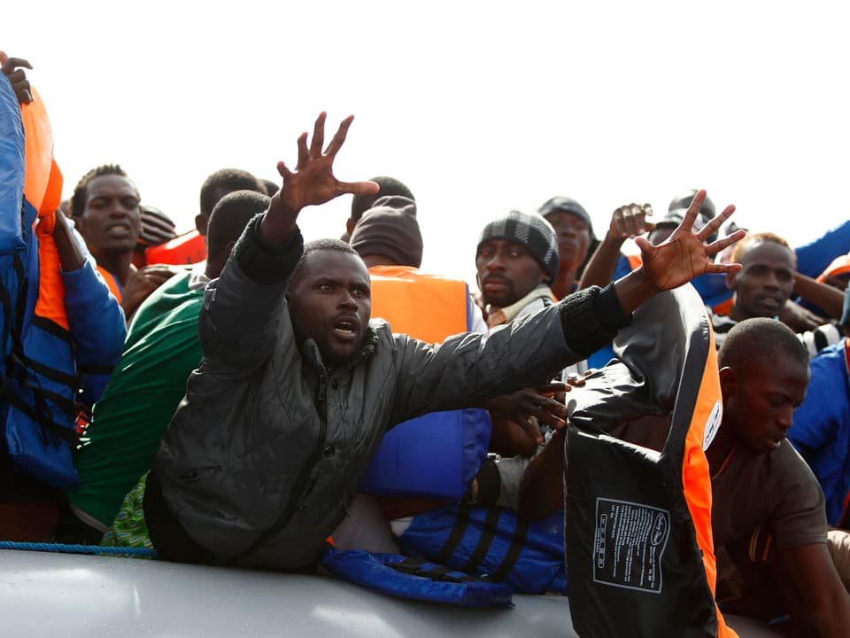 Flüchtlinge auf einem Boot strecken ihre Arme den Helfern entgegen.
