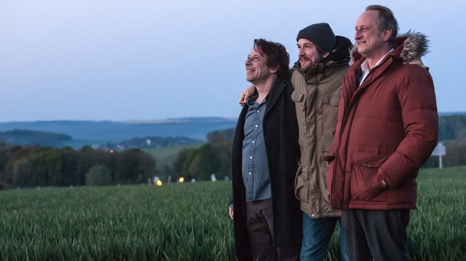 Drei lachende Männer stehen in einem Feld.