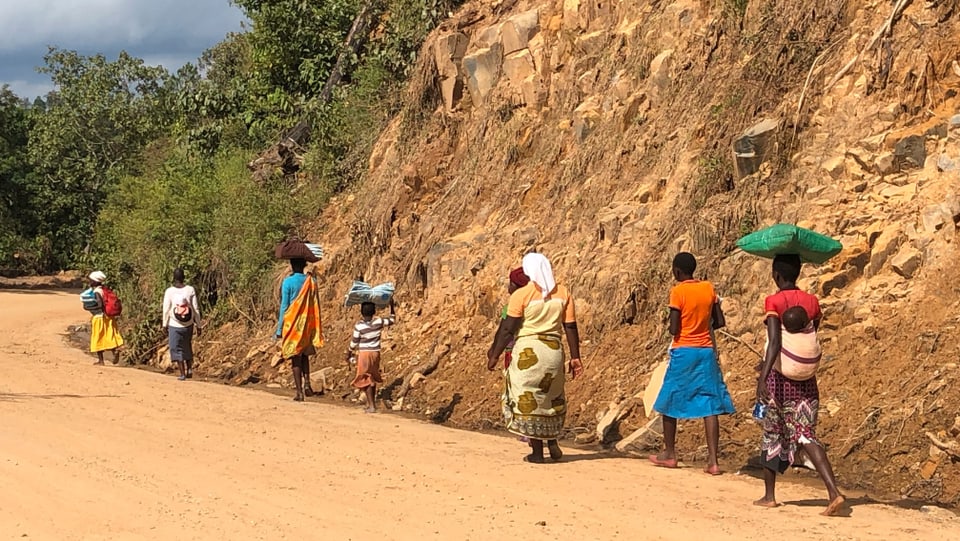 Eine Gruppe von Frauen und Kindern geht einer Strasse entlang und trägt erhaltene Moskitonetze