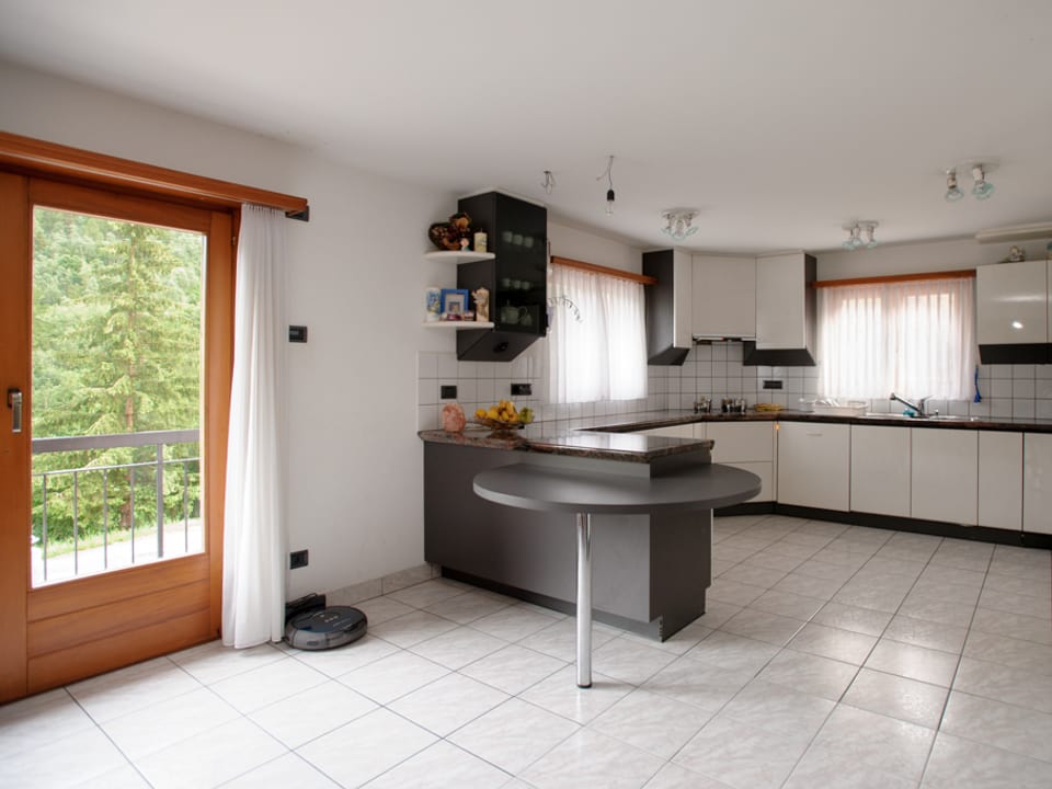 Blick in die grosse Küche mit weisser und anthrazitfarbener Einrichtung und einer grossen Tür, die auf die Terrasse führt.