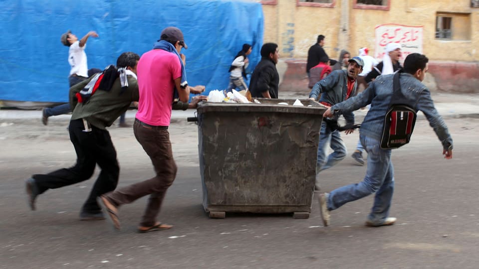 Junge Männer schieben einen Abfallcontainer durch die Strassen Alexandrias.