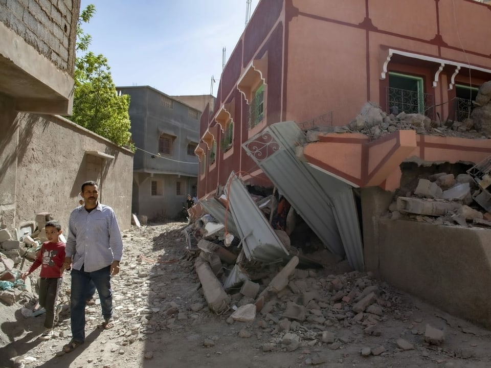 Ein Mann geht mit einem Buben an der Hand an einem zerstörten Gebäude vorbei.