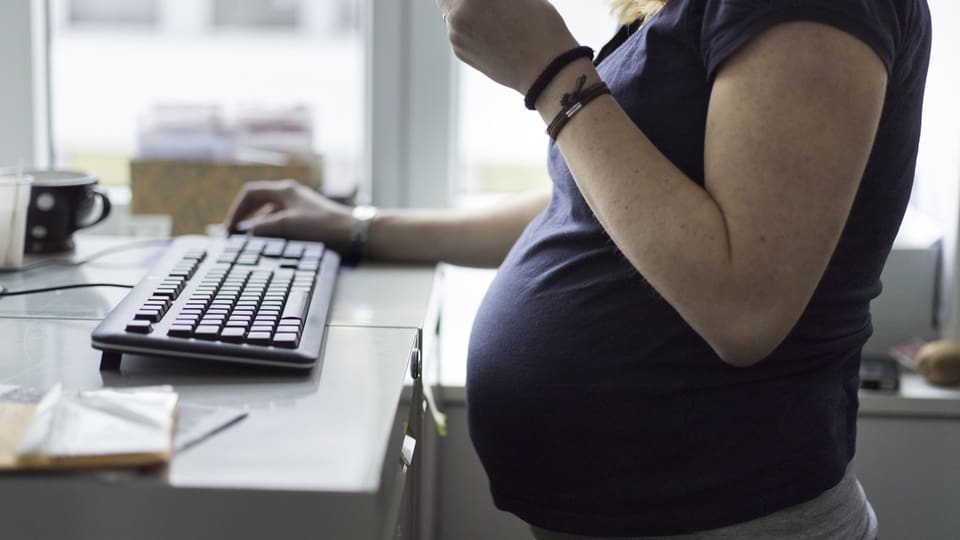 Schwangere Frau mit Bauch steht an einem Pult mit Tastatur