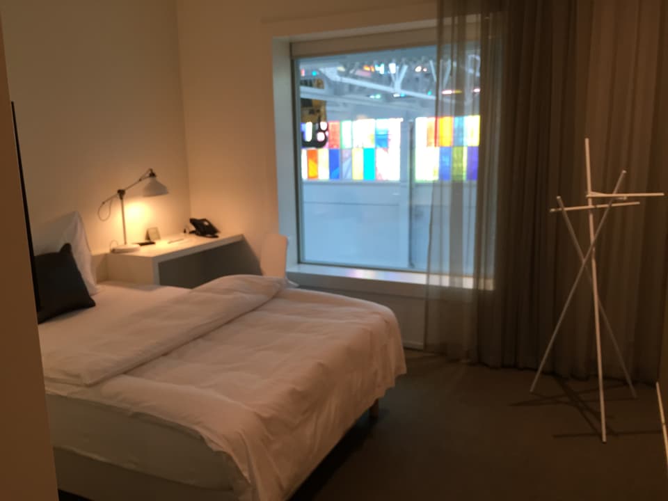 Hotelzimmer mit Bett und Nachtisch und farbigem Fenster.