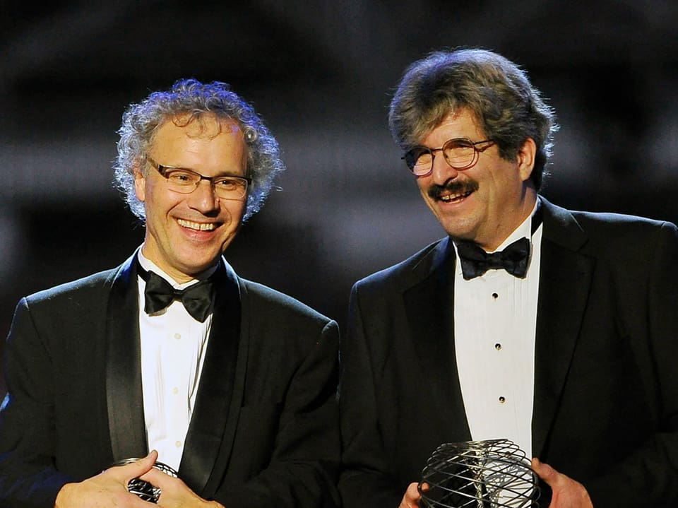 Dois homens de smoking com troféus.