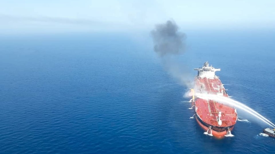 Roter Öltanker im blauen Meer wird mit Wassers aus Löschschiffen besprüht.
