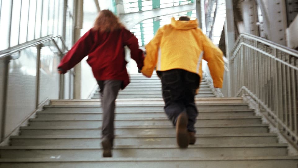 Zwei Personen rennen Hand in Hand eine Treppe hoch