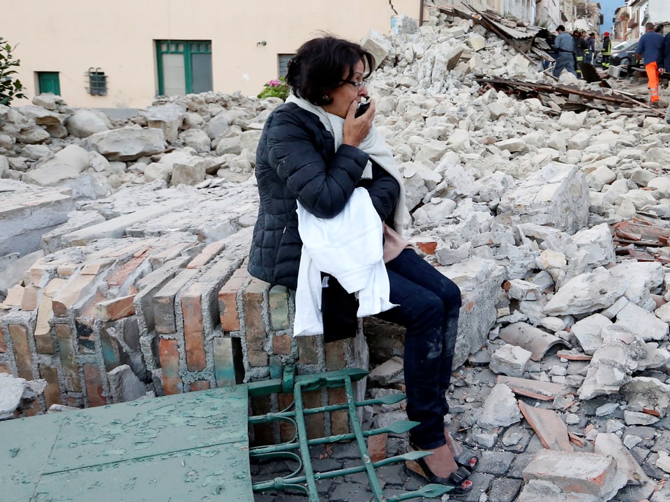 Frau sitzt schockiert vor Trümmern eines Hauses