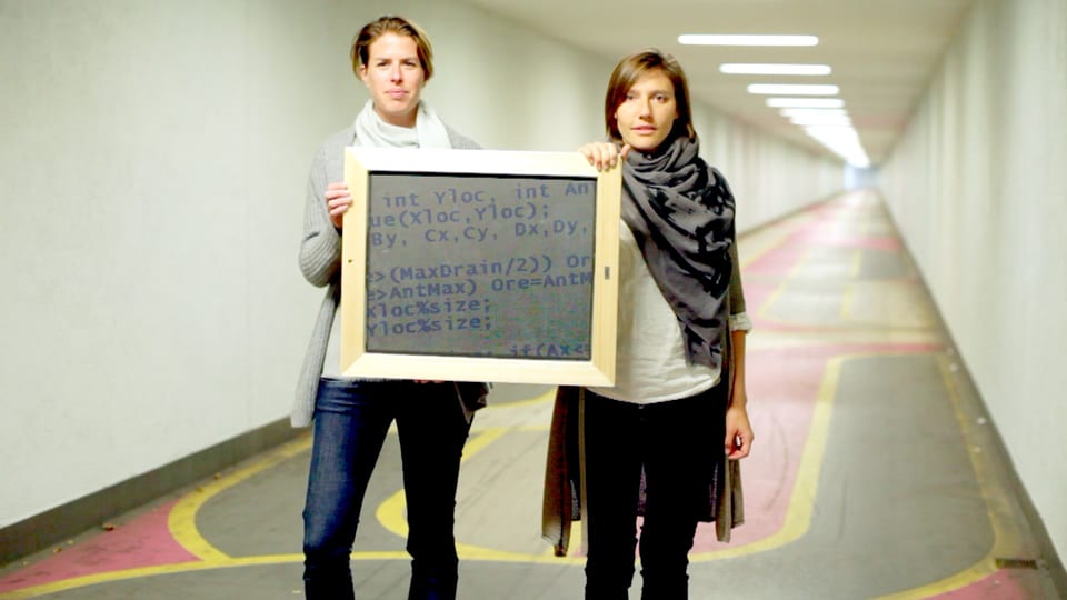 Maya Baas und Terry Harker halten in einem Gang ein Schild mit Code.