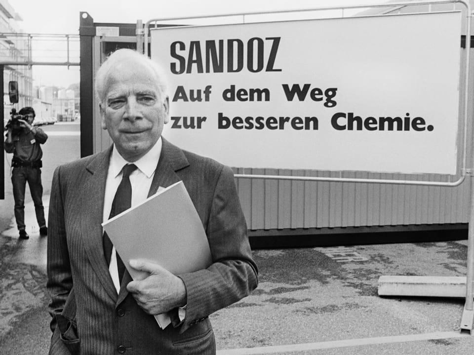 Schwarzweiss Foto Marc von Moret vor einem Sandoz-Plakat