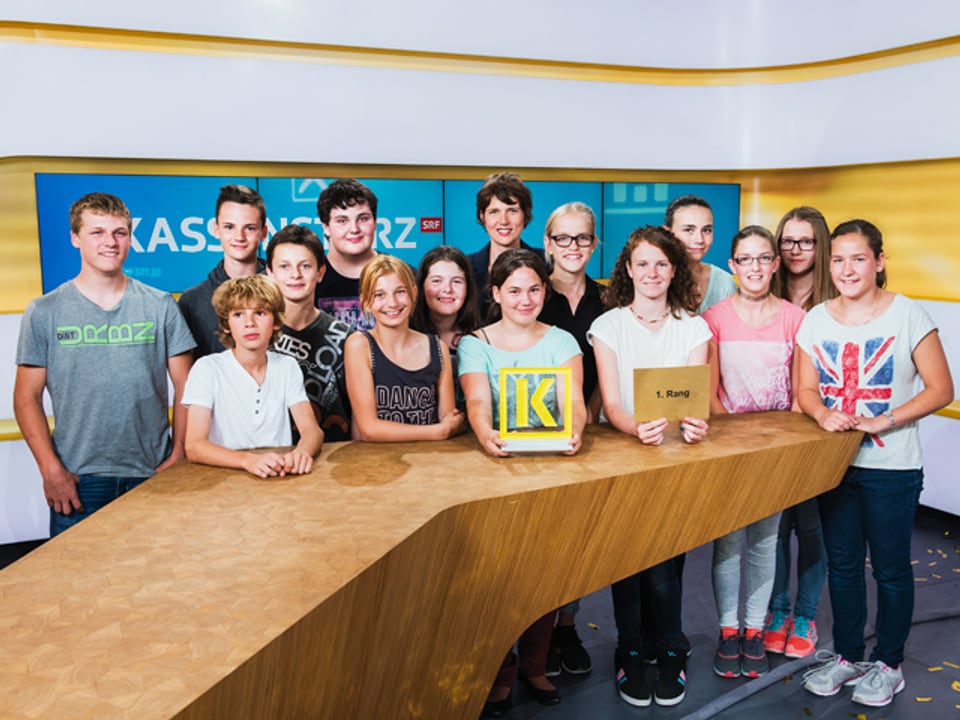 14 Jugendliche mit Moderatorin Kathrin Winzenried im Kassensturzstudio.