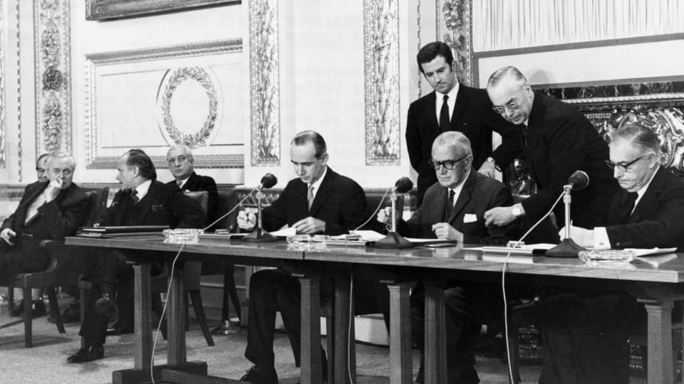 Ein Schwarzweiss -Foto: Männer sitzen an einem Tisch und Unterschreiben einen Vertrag.