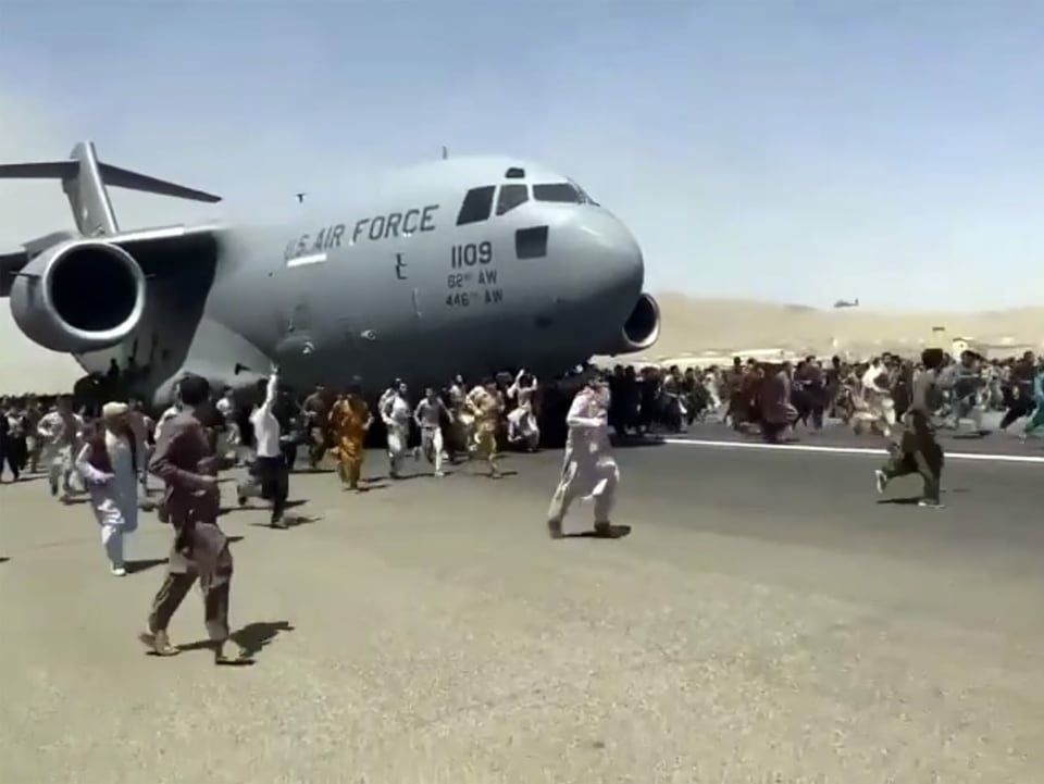 Ein unglaubliches Bild: Während die Flugmaschine der U.S. Airforce auf der Startbahn beschleunigt, rennen hunderte Menschen der Flugmaschine nach, um offenbar auf sie draufzuklettern.