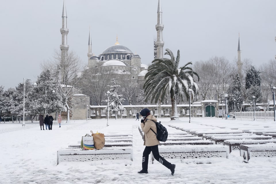 Eine Frau läuft durch den Schnee in Istanbul. Dahinter ist die Sultan Ahmet Moschee zu sehen. 