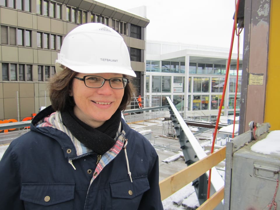 Stadträtin Pearl Pedergnana mit blauer Jacke und weissem Baustellenhelm vor einem Stahlträger.