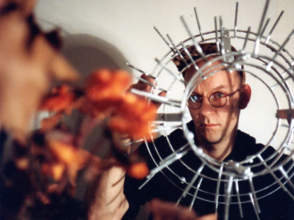 Ein Amnn mit Brille schaut durch ein rundes Objekt aus Metall in die Kamera.