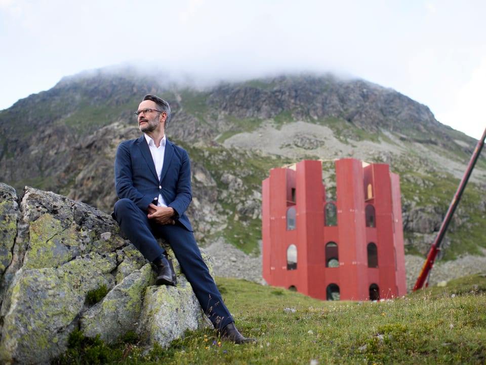 Berglandschaft mit rotem Turm, davor sitzt Giovanni Netzer auf einem Stein