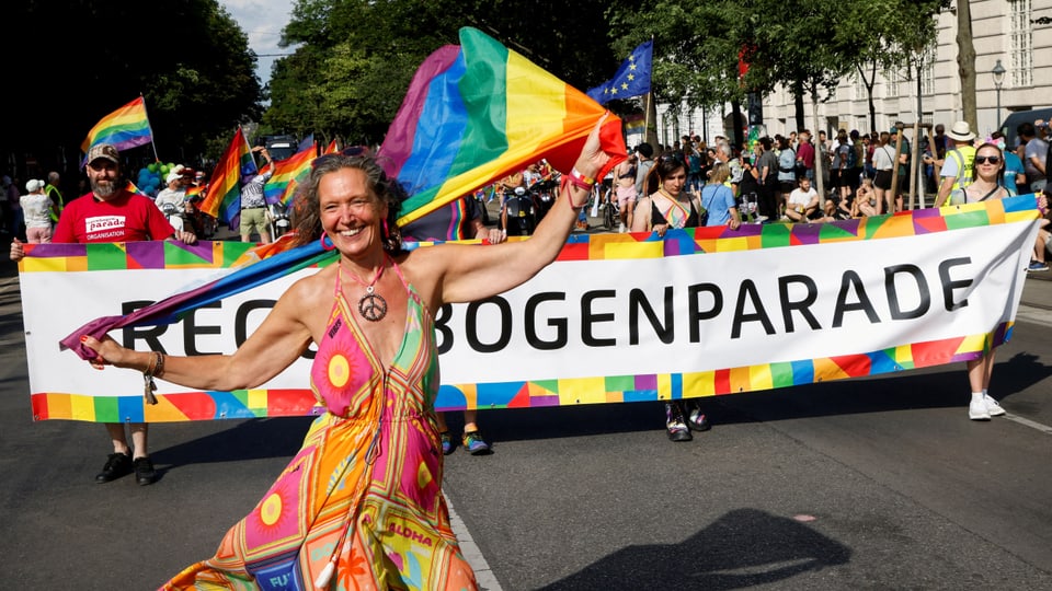 Frau mit Pride-Fahne geht vor einem «Regenbogenparade»-Banner.