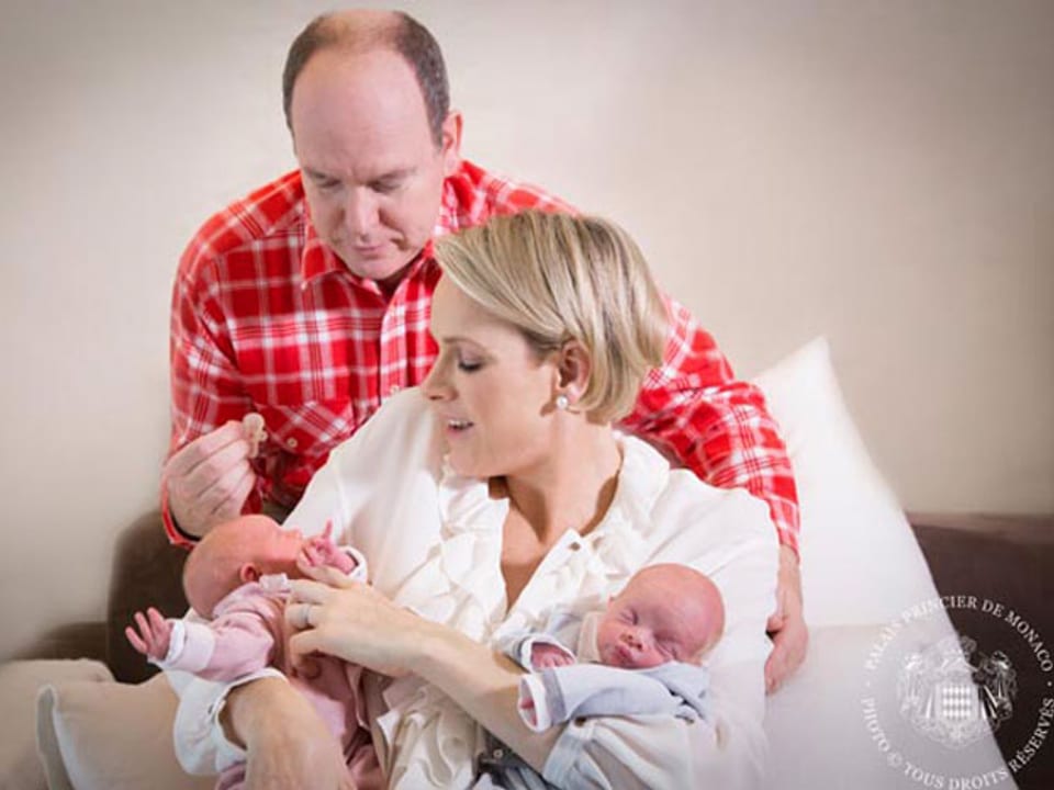 Prinz Albert in rot-weiss-karriertem Hemd, Prinzessin Charlàne in weiss hält die Zwillinge in den Armen