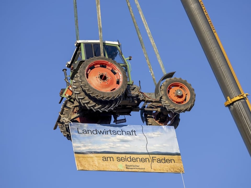 A tractor carrying a banner is pulled on a crane.