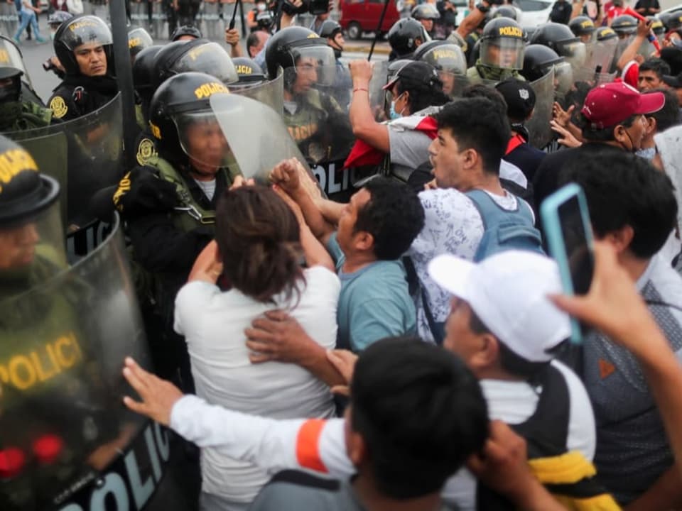 Wütende Menschenmenge in Cusco verdrängt eine Polizeireihe.