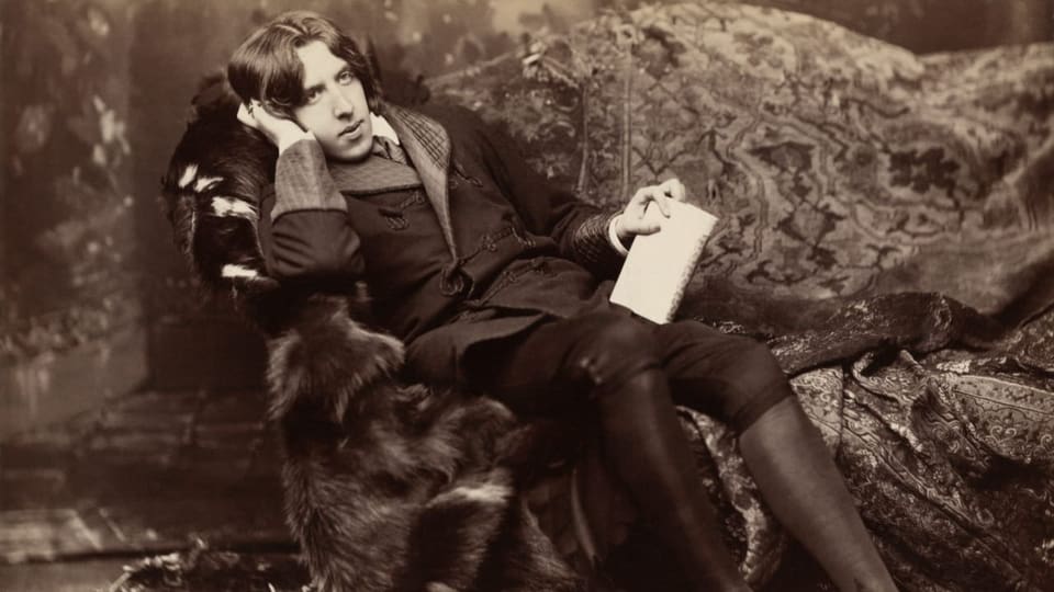 Schwarzweissaufnahme: Eleganter Mann in kniehosen Stiefeln sitzt gedankenverloren auf Sofa (Oscar Wilde)