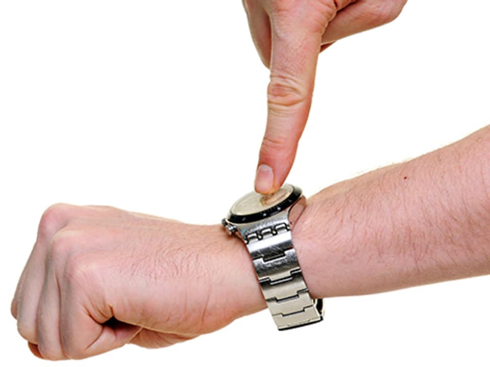 Ein Mann zeigt mit seinem Zeigefinger auf seine Armbanduhr.