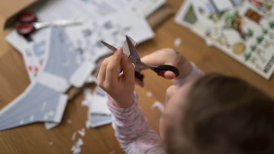 Kind schneidet Papier mit einer Schere.