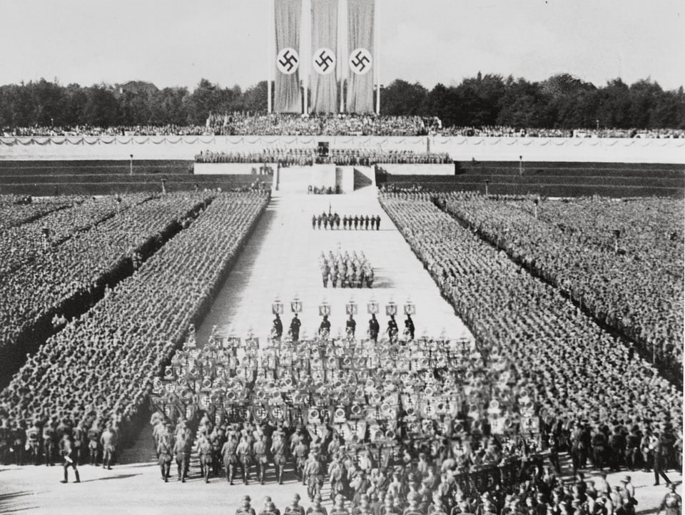 Filmstill aus «Triumph des Willens». Menschenmassen stehen bei einer Parade, im Hintergrund wehen Nazi-Flaggen.