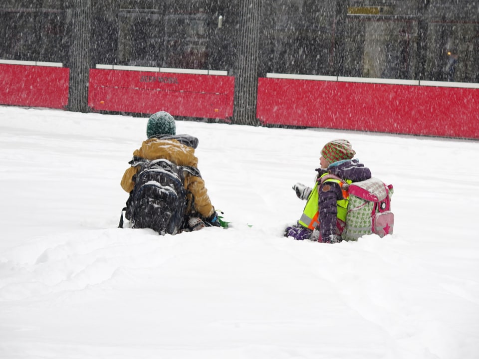 Kinder sitzen im Schnee, im Hintergrund ein Tram