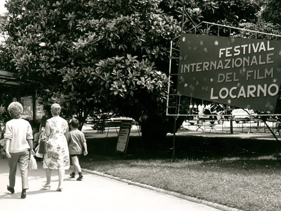 Black and white shot: Several people walk through a film festival advertising banner