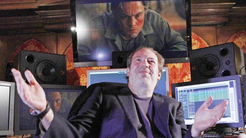 Ein Mann mittleren Alters sitzt in einem Tonstudio mit mehreren Bildschirmen, Lautsprechern und gestikuliert