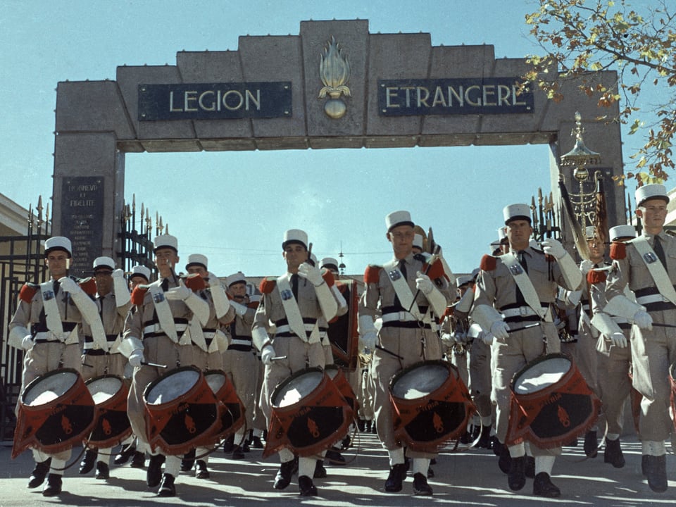 Farbfoto einer Militärparade vor einem Tor mit der Aufschrift "Legion etrangere"