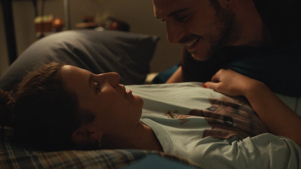 A woman cuddles with her boyfriend on the bed.